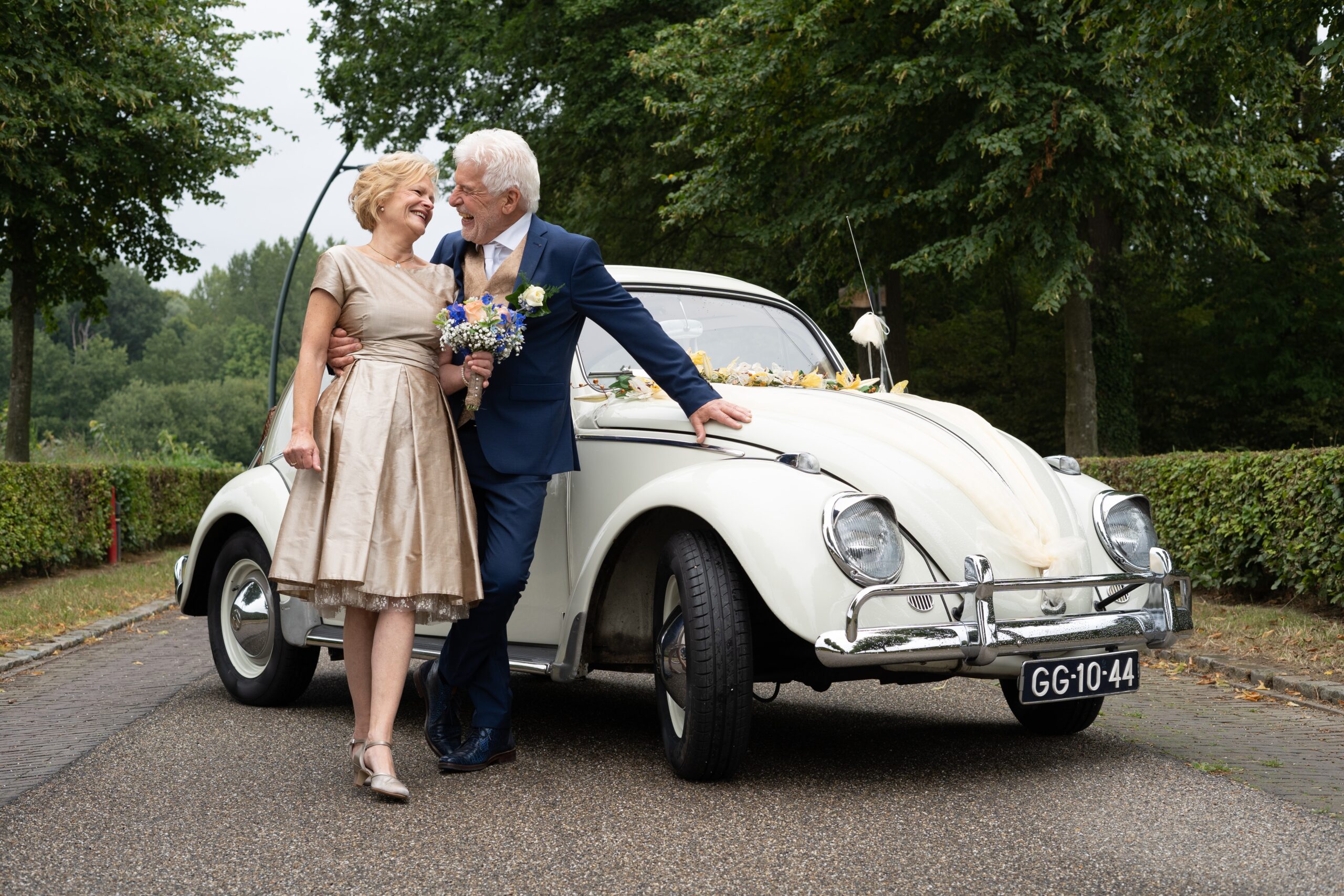 older married couple taking a picture by a Volkswagen Beetle